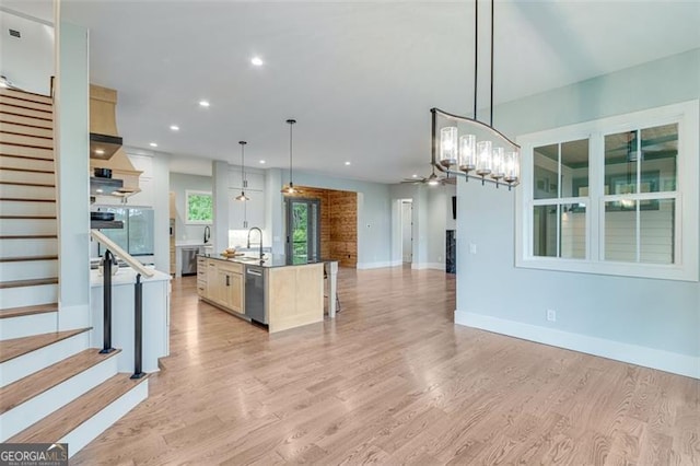 kitchen featuring a center island with sink, decorative light fixtures, sink, and light hardwood / wood-style flooring