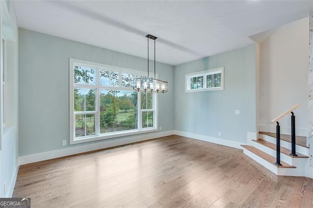 unfurnished dining area featuring a notable chandelier, a wealth of natural light, and hardwood / wood-style flooring