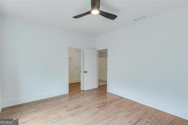 unfurnished bedroom with light hardwood / wood-style floors, a closet, a walk in closet, and ceiling fan