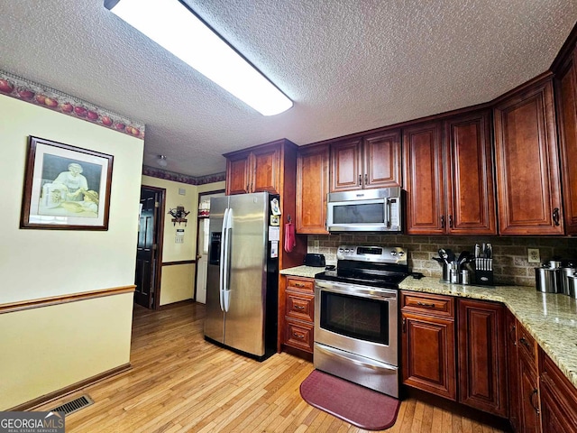 kitchen featuring a textured ceiling, backsplash, appliances with stainless steel finishes, light stone countertops, and light hardwood / wood-style floors