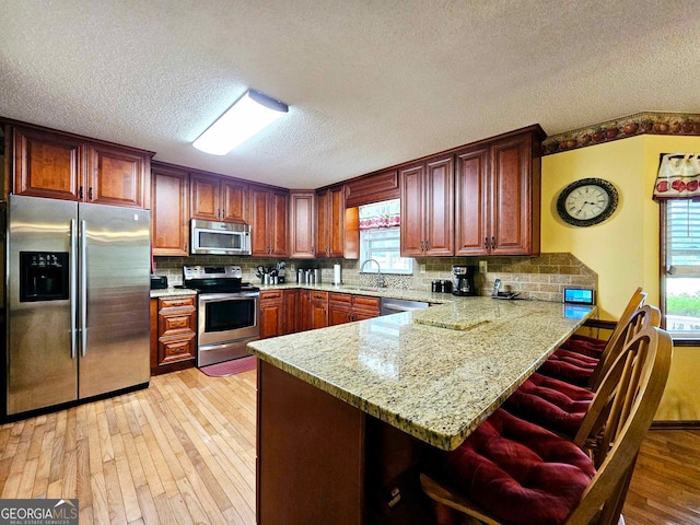 kitchen featuring stainless steel appliances, plenty of natural light, kitchen peninsula, and light hardwood / wood-style flooring