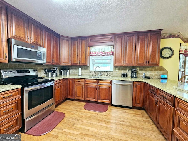 kitchen with sink, a textured ceiling, appliances with stainless steel finishes, light stone countertops, and light hardwood / wood-style floors