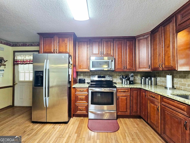 kitchen with light stone countertops, appliances with stainless steel finishes, tasteful backsplash, and light hardwood / wood-style flooring