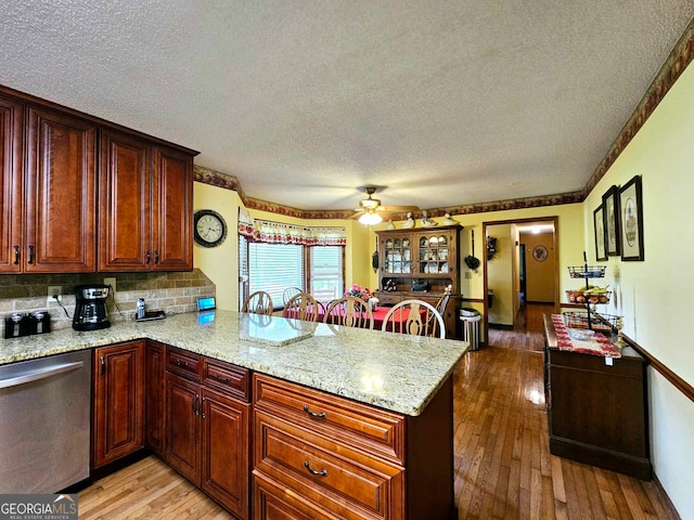 kitchen featuring light hardwood / wood-style floors, kitchen peninsula, light stone countertops, a textured ceiling, and stainless steel dishwasher