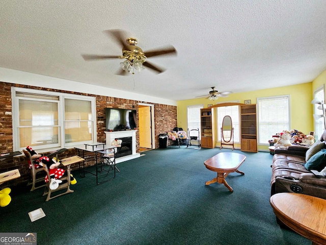 carpeted living room with a textured ceiling, a large fireplace, ceiling fan, and brick wall