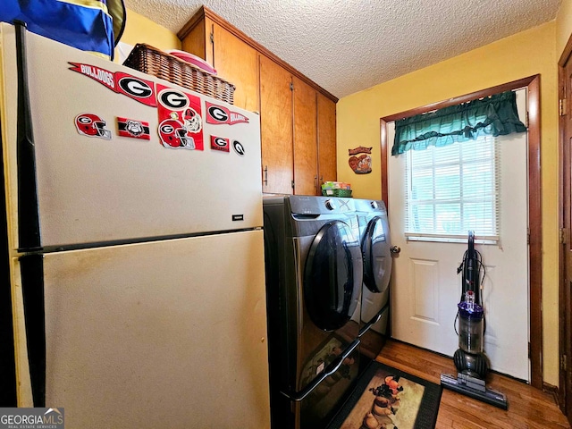 clothes washing area with washing machine and clothes dryer, light wood-type flooring, a textured ceiling, and cabinets