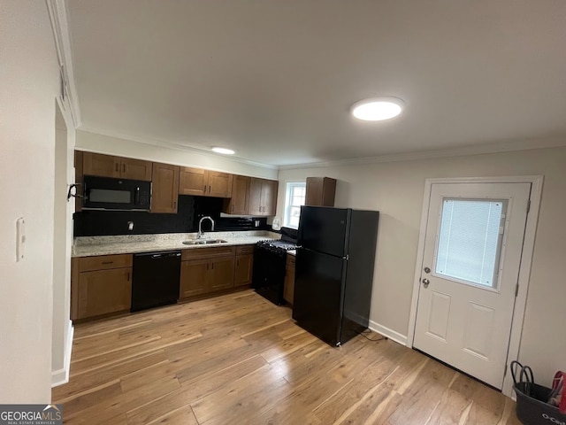 kitchen with ornamental molding, light wood-type flooring, sink, and black appliances