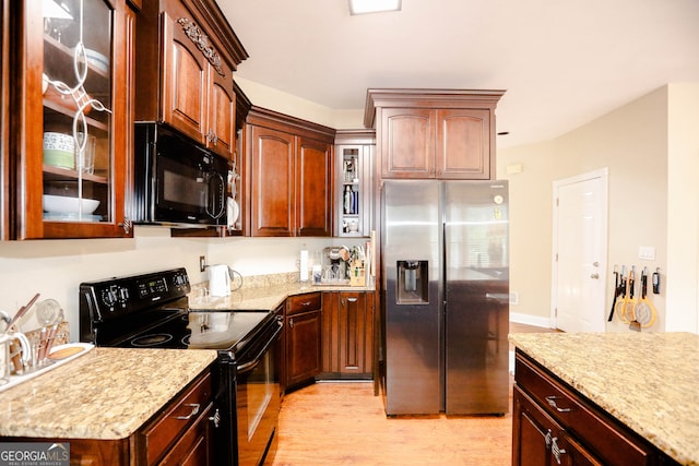 kitchen with light stone countertops, light hardwood / wood-style floors, and black appliances