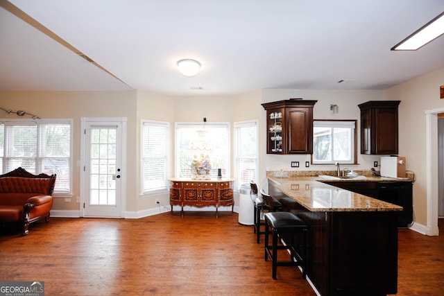 kitchen featuring light stone counters, dark brown cabinets, decorative light fixtures, a kitchen breakfast bar, and dark hardwood / wood-style flooring