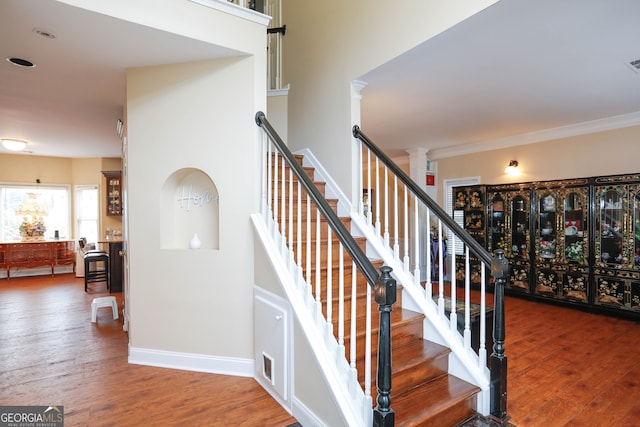 stairway featuring wood-type flooring, crown molding, and ornate columns