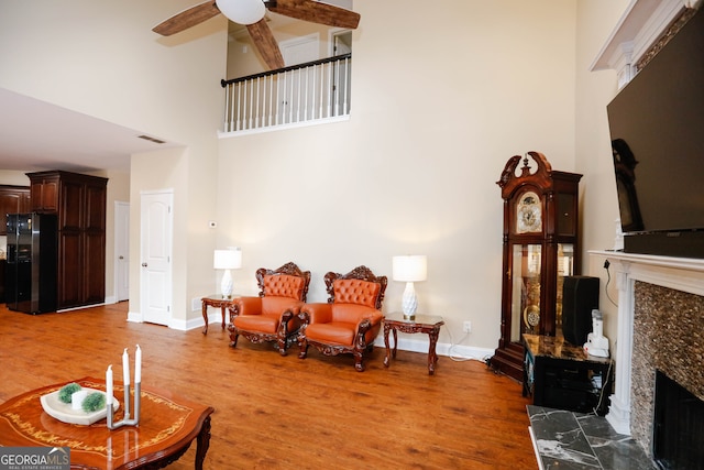 living room with ceiling fan, hardwood / wood-style flooring, a fireplace, and a high ceiling