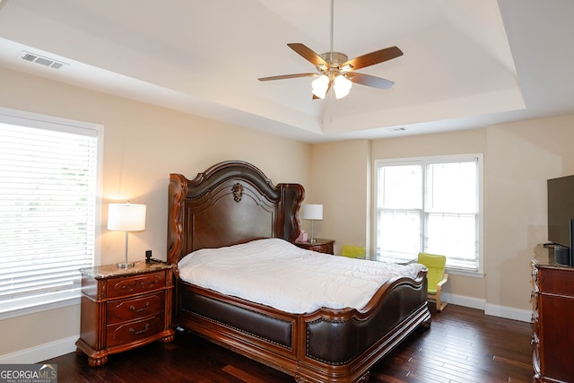 bedroom with a raised ceiling, dark hardwood / wood-style floors, and ceiling fan