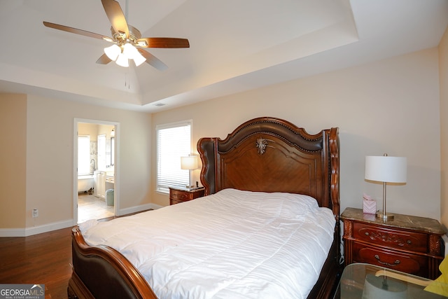 bedroom with ceiling fan, a raised ceiling, ensuite bathroom, and hardwood / wood-style floors