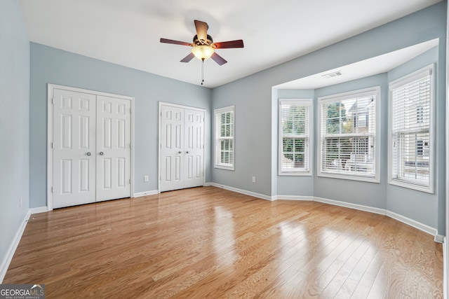 unfurnished bedroom featuring light hardwood / wood-style flooring, two closets, and ceiling fan