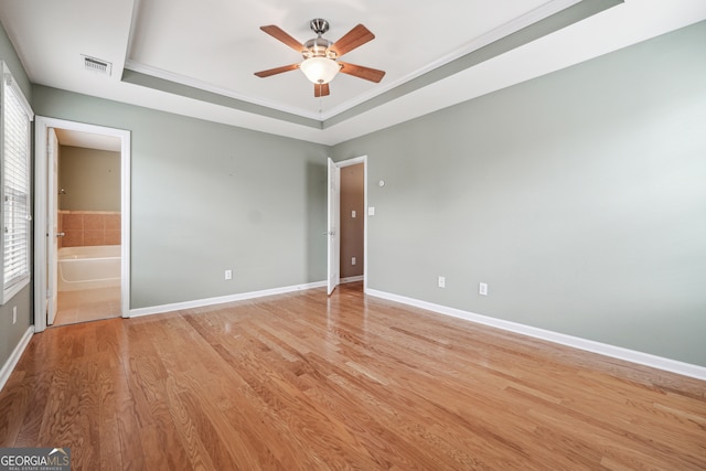 empty room with light hardwood / wood-style flooring, ceiling fan, and a raised ceiling