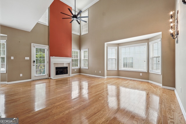 unfurnished living room featuring a tile fireplace, a high ceiling, ornamental molding, and light hardwood / wood-style flooring