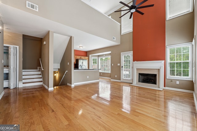 unfurnished living room with light hardwood / wood-style floors, ceiling fan, a premium fireplace, and high vaulted ceiling