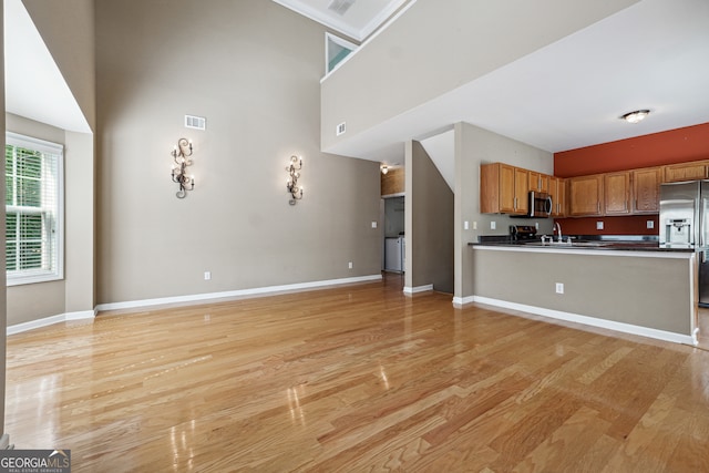 kitchen with sink, kitchen peninsula, stainless steel appliances, a high ceiling, and light wood-type flooring