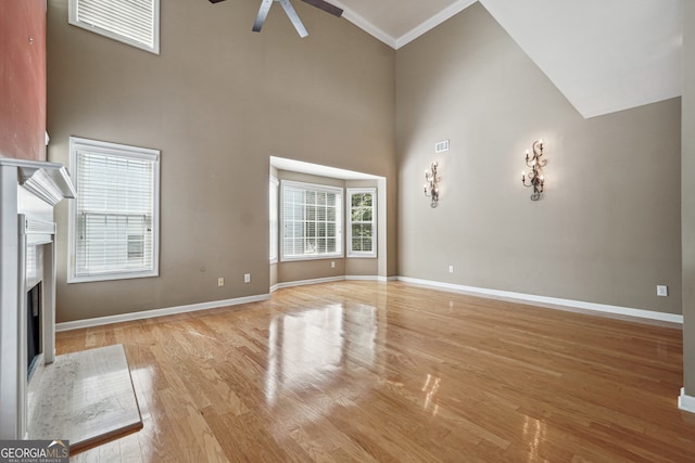 unfurnished living room featuring ceiling fan, ornamental molding, light hardwood / wood-style floors, and high vaulted ceiling