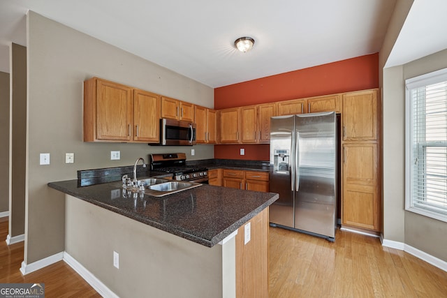 kitchen featuring sink, kitchen peninsula, stainless steel appliances, dark stone countertops, and light wood-type flooring