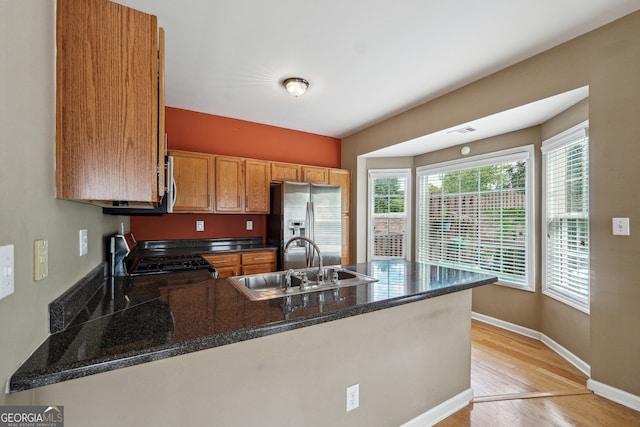 kitchen featuring kitchen peninsula, sink, light hardwood / wood-style flooring, stainless steel refrigerator with ice dispenser, and black stove