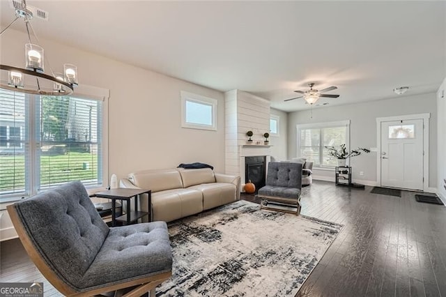 living room featuring ceiling fan with notable chandelier, a fireplace, and dark hardwood / wood-style flooring