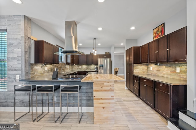 kitchen with stainless steel fridge with ice dispenser, a peninsula, island exhaust hood, and dark brown cabinets