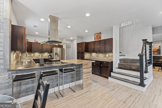 kitchen with island range hood, stainless steel refrigerator with ice dispenser, dark brown cabinets, and backsplash