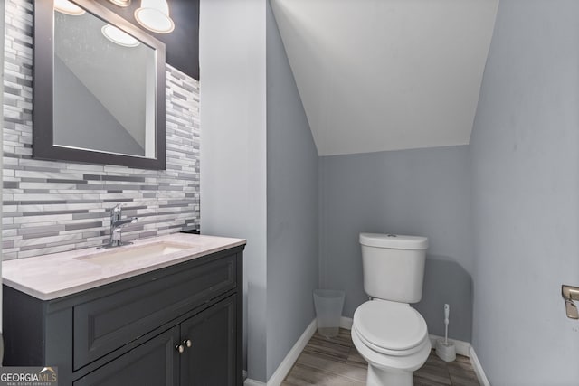 bathroom with vanity, lofted ceiling, toilet, and tasteful backsplash