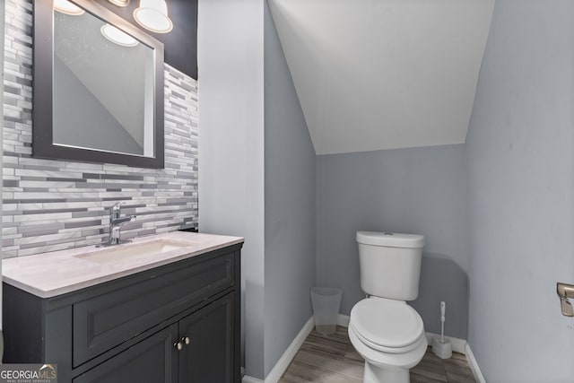bathroom with tasteful backsplash, baseboards, toilet, vanity, and vaulted ceiling