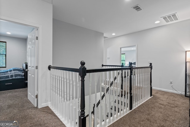 corridor with visible vents, an upstairs landing, plenty of natural light, and carpet floors