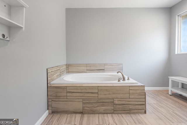 bathroom with a bath, wood finished floors, and baseboards