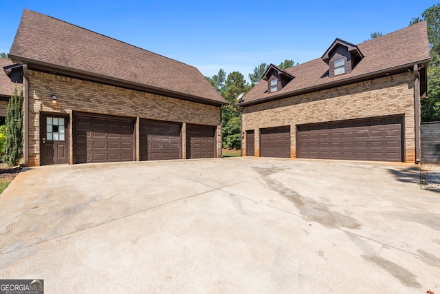 view of home's exterior with brick siding, a shingled roof, a garage, and driveway