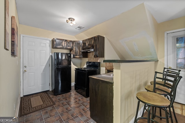 kitchen featuring dark brown cabinetry, backsplash, a breakfast bar, and black appliances