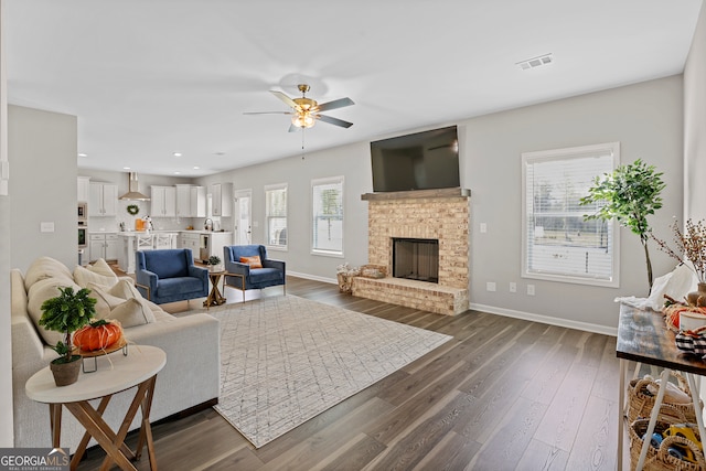 living room with a fireplace, ceiling fan, and dark wood-type flooring