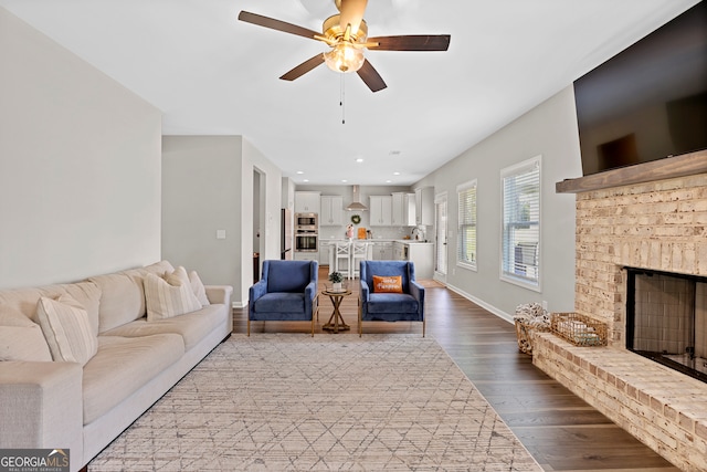 living room featuring a brick fireplace, light wood-type flooring, sink, and ceiling fan