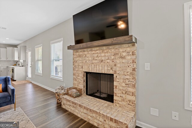 living room with a brick fireplace, sink, and dark wood-type flooring