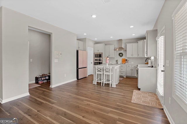 kitchen featuring a kitchen island, wall chimney exhaust hood, a kitchen bar, stainless steel appliances, and hardwood / wood-style floors