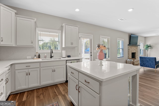 kitchen featuring white cabinets, sink, a kitchen island, hardwood / wood-style flooring, and a fireplace