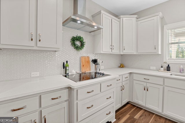 kitchen with dark wood-type flooring, white cabinets, wall chimney range hood, backsplash, and black electric cooktop