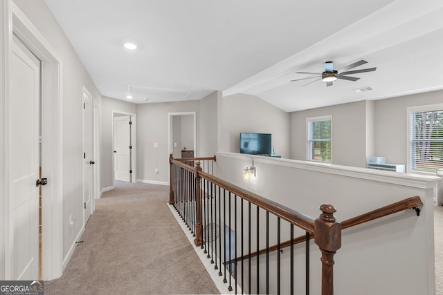 hallway with a wealth of natural light, vaulted ceiling, and light colored carpet