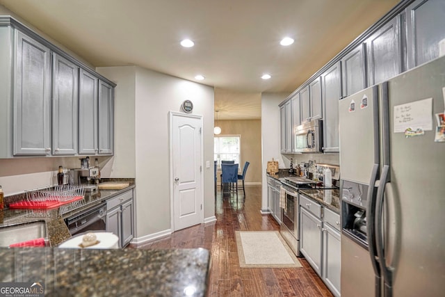 kitchen featuring stainless steel appliances, dark hardwood / wood-style floors, dark stone counters, and gray cabinetry