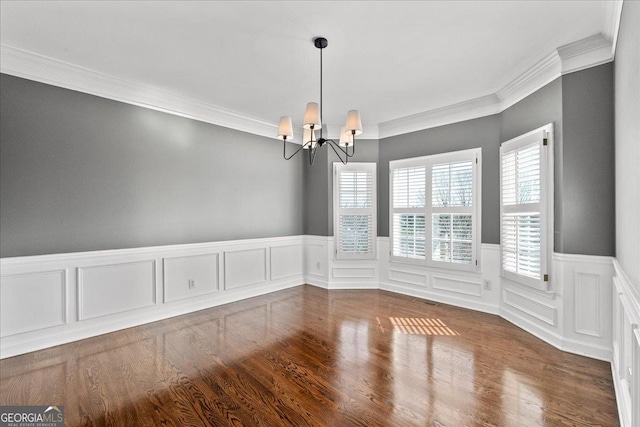 unfurnished dining area featuring a chandelier, ornamental molding, wainscoting, and wood finished floors