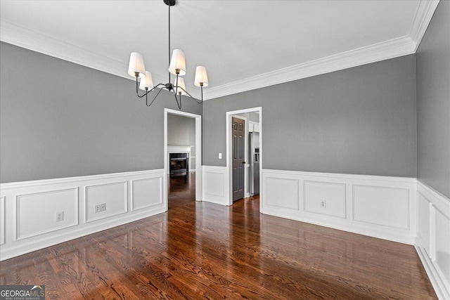 unfurnished dining area with crown molding, a fireplace, a notable chandelier, and wood finished floors