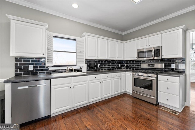 kitchen with stainless steel appliances, dark countertops, a sink, and dark wood finished floors