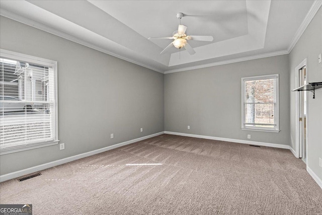 carpeted empty room featuring a ceiling fan, a tray ceiling, visible vents, and baseboards