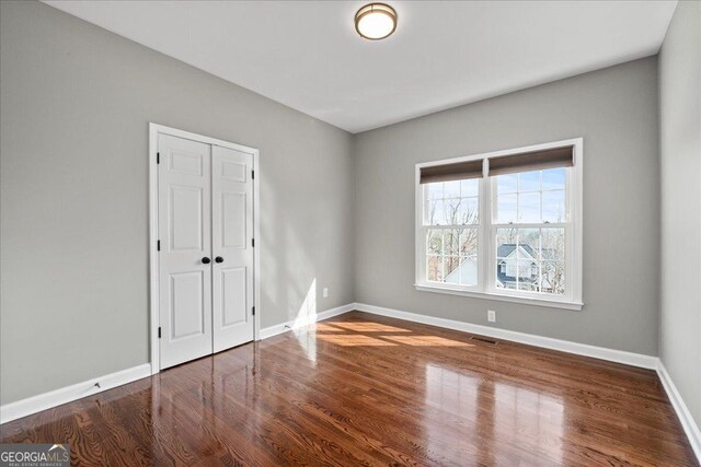 unfurnished bedroom featuring a closet, wood finished floors, visible vents, and baseboards