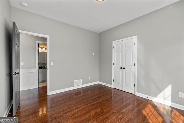 unfurnished bedroom with a closet, wood finished floors, visible vents, and baseboards