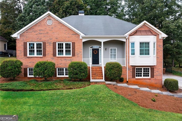 view of front of house with a porch, brick siding, a front lawn, and a chimney