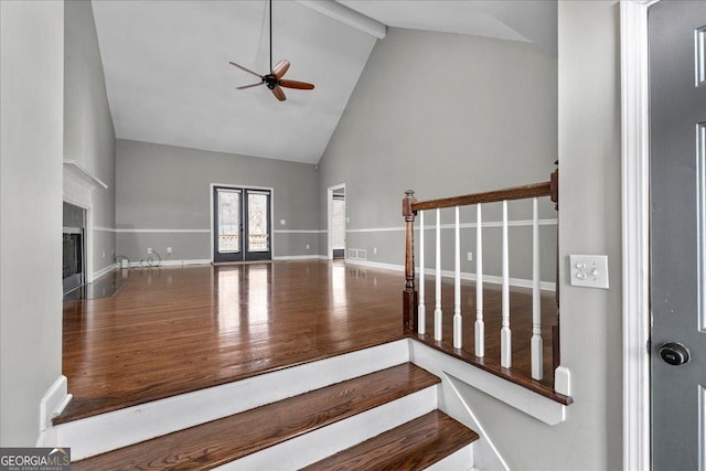 unfurnished living room with ceiling fan, high vaulted ceiling, wood finished floors, a fireplace with flush hearth, and stairs